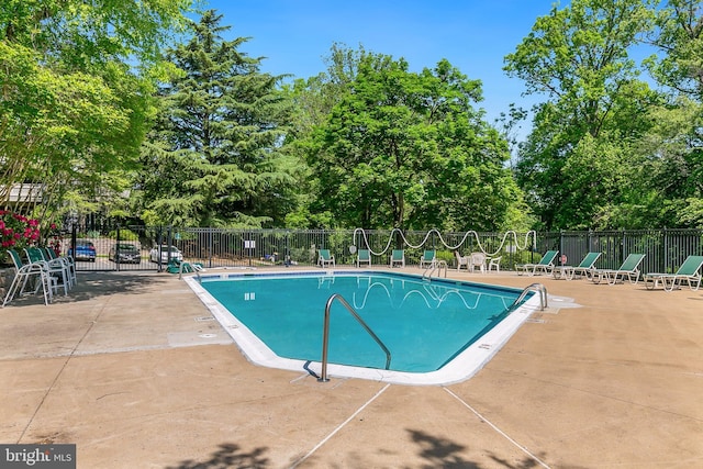 community pool featuring fence, a patio area, and view of scattered trees