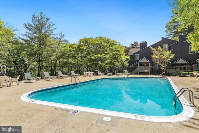 community pool with fence, a patio, and view of scattered trees
