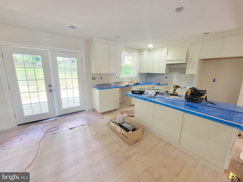 kitchen with light wood-type flooring, a center island, tasteful backsplash, white cabinetry, and french doors