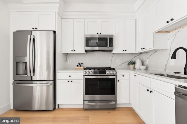kitchen featuring appliances with stainless steel finishes, tasteful backsplash, a sink, white cabinets, and light wood-type flooring