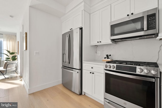 kitchen featuring light wood-style flooring, white cabinetry, light countertops, appliances with stainless steel finishes, and tasteful backsplash