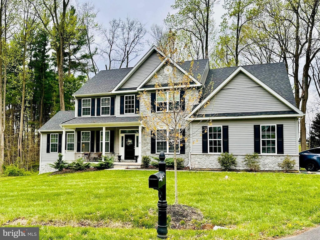 view of front of house featuring covered porch, stone siding, and a front yard