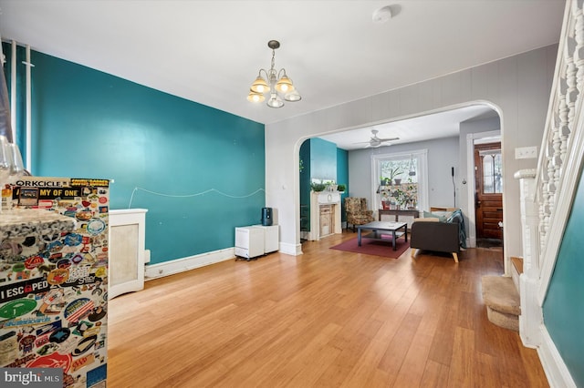 interior space featuring stairs, ceiling fan with notable chandelier, wood finished floors, arched walkways, and baseboards