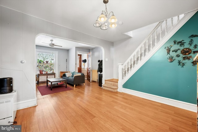 living room with wood finished floors, ceiling fan with notable chandelier, stairway, baseboards, and arched walkways
