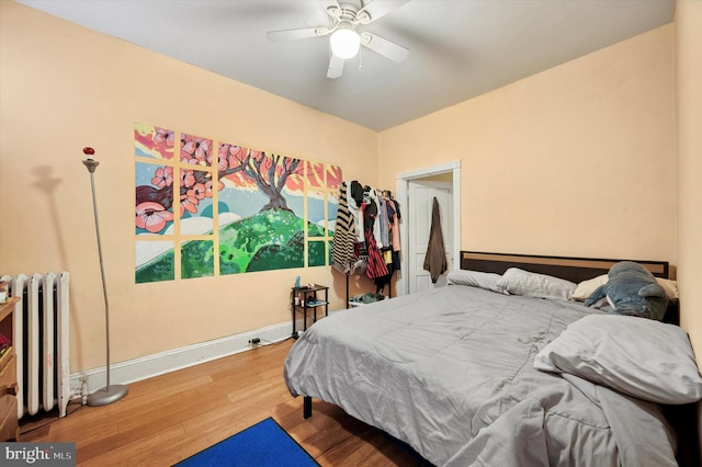 bedroom featuring a ceiling fan, wood finished floors, baseboards, and radiator heating unit