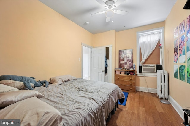 bedroom with baseboards, radiator, cooling unit, ceiling fan, and wood finished floors