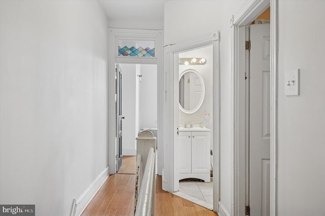 corridor featuring baseboards, light wood-style flooring, and a sink
