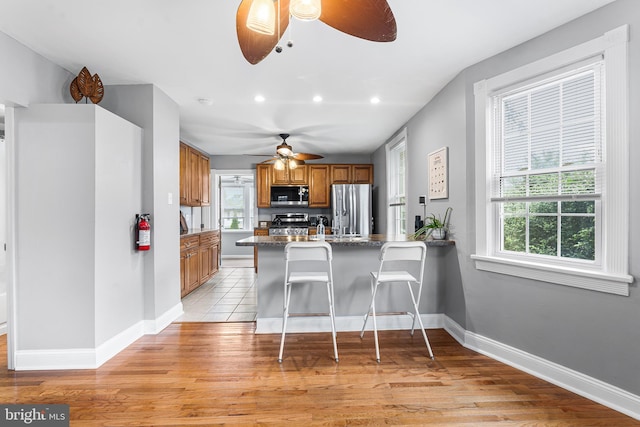 kitchen featuring stainless steel appliances, ceiling fan, brown cabinets, a peninsula, and light wood-style flooring