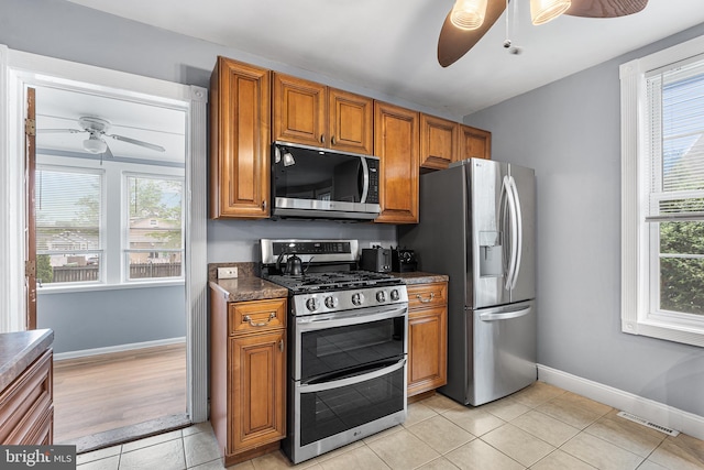 kitchen featuring stainless steel appliances, ceiling fan, brown cabinetry, and dark countertops