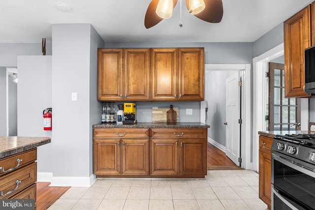 kitchen with double oven range, a ceiling fan, brown cabinetry, and baseboards