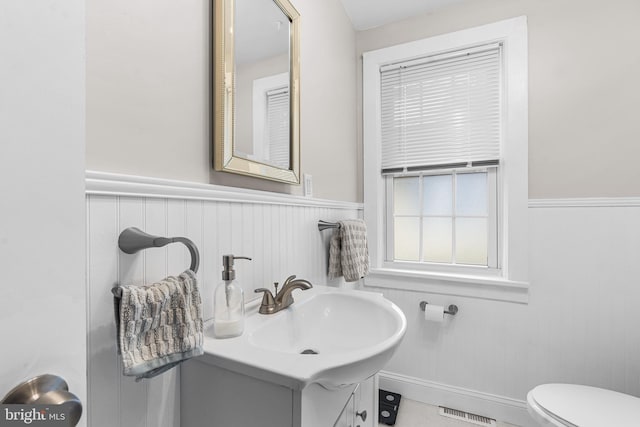 bathroom featuring a wainscoted wall, toilet, and vanity