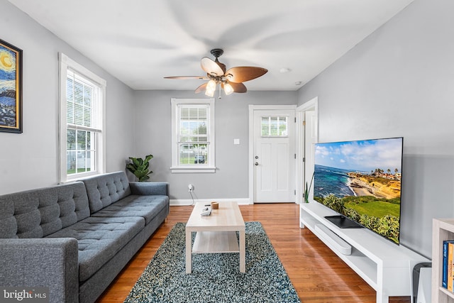 living area with wood finished floors, a ceiling fan, and baseboards