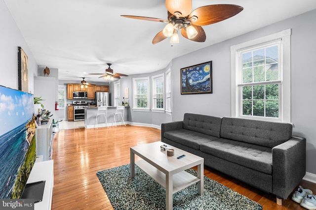 living room featuring ceiling fan, light wood finished floors, and baseboards