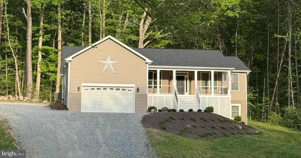 view of front of property with a wooded view, a garage, stairway, a porch, and gravel driveway
