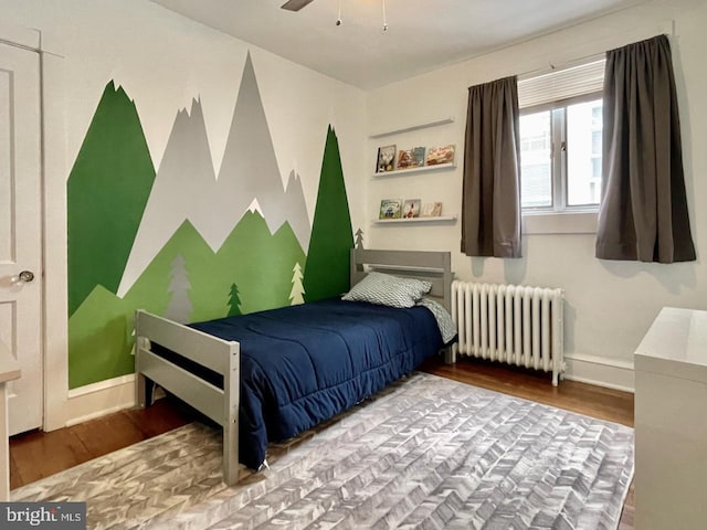 bedroom with radiator, wood finished floors, and baseboards