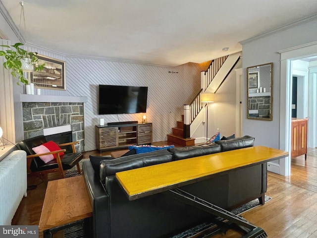 living room featuring stairway, crown molding, wood finished floors, a stone fireplace, and an accent wall