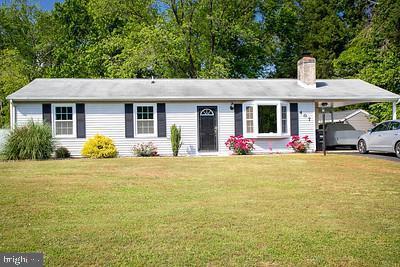 ranch-style home featuring a chimney, a front yard, and an attached carport