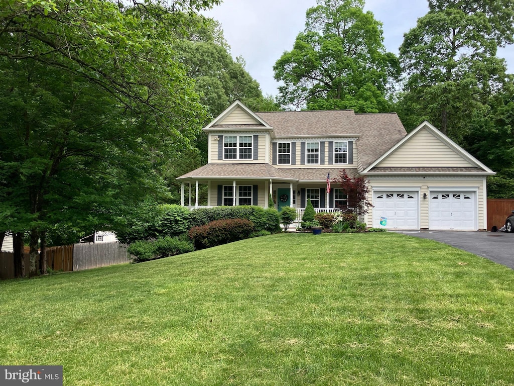 colonial house featuring driveway, fence, an attached garage, a front yard, and a porch