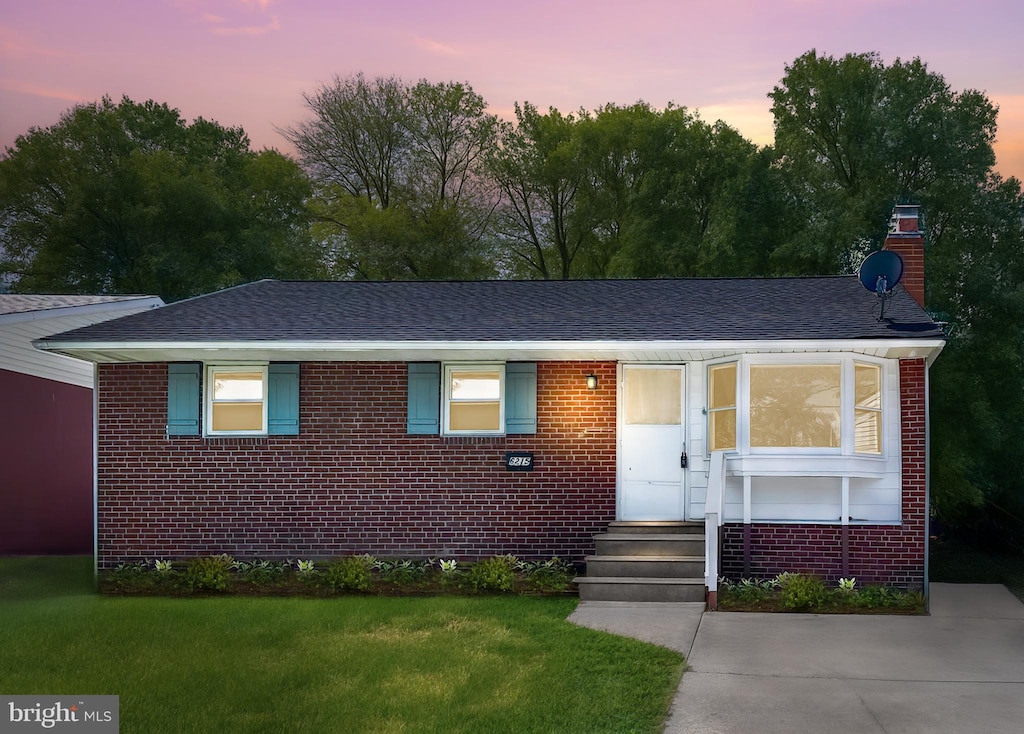 ranch-style house with brick siding, a shingled roof, a chimney, and a front yard