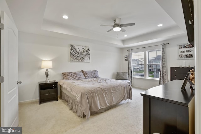 bedroom featuring a raised ceiling, light colored carpet, recessed lighting, baseboards, and ceiling fan