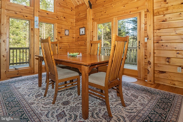 dining space with lofted ceiling, wooden walls, a healthy amount of sunlight, and wood finished floors