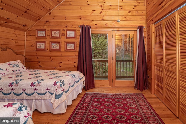 bedroom with vaulted ceiling, wooden walls, light wood-style floors, and access to exterior