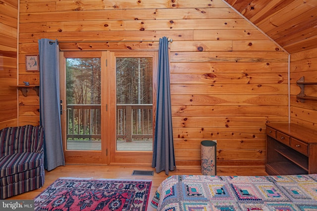 unfurnished bedroom with lofted ceiling, visible vents, wooden walls, access to outside, and wood finished floors