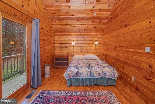 bedroom with wood walls, lofted ceiling, visible vents, and wood finished floors