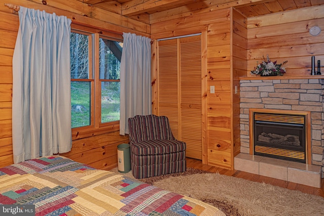 bedroom featuring a stone fireplace, wooden walls, a closet, and wood finished floors
