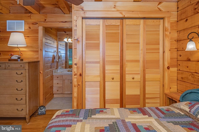 bedroom with wood walls, a closet, visible vents, connected bathroom, and light wood-style floors