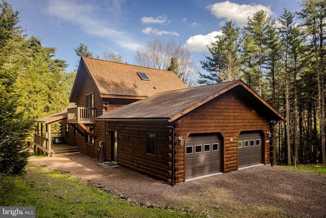 view of home's exterior featuring a detached garage, a wooden deck, a shingled roof, and log exterior