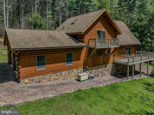rear view of property featuring log siding, a shingled roof, cooling unit, and a view of trees
