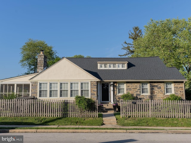 view of front of house featuring stone siding, a fenced front yard, a chimney, a sunroom, and roof with shingles