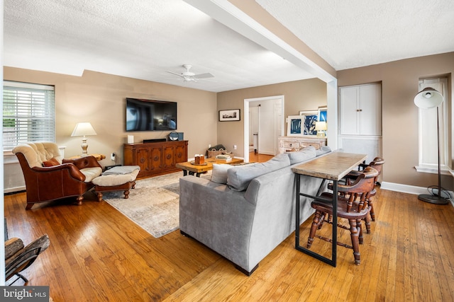 living room featuring hardwood / wood-style floors, ceiling fan, baseboards, and a textured ceiling