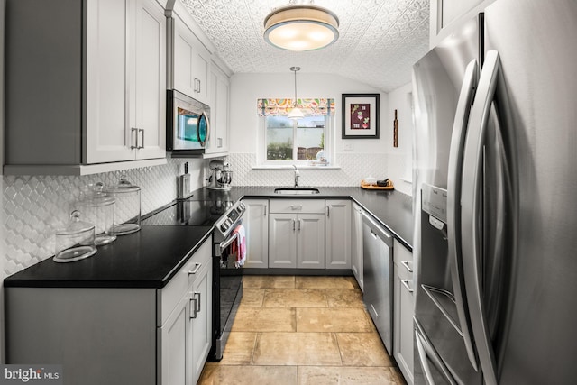 kitchen featuring stainless steel appliances, a sink, dark countertops, decorative backsplash, and stone tile floors