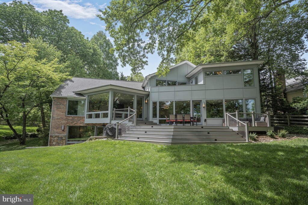 rear view of property featuring a sunroom, a deck, a yard, brick siding, and roof with shingles