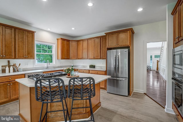 kitchen with stainless steel appliances, a sink, brown cabinetry, light countertops, and light wood-style flooring