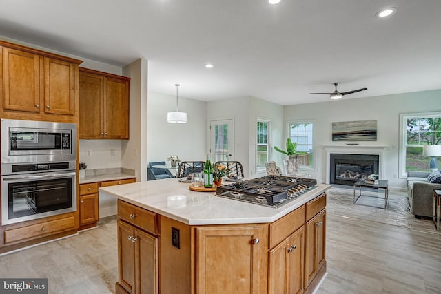 kitchen with stainless steel appliances, open floor plan, light wood-style floors, light countertops, and a ceiling fan