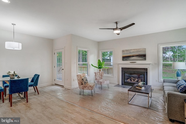 living area featuring plenty of natural light, a ceiling fan, baseboards, and a fireplace with flush hearth