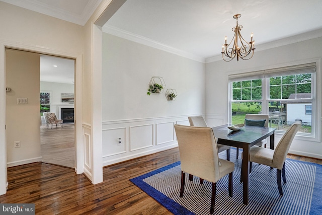 dining space featuring a chandelier, dark wood finished floors, crown molding, a wainscoted wall, and a glass covered fireplace
