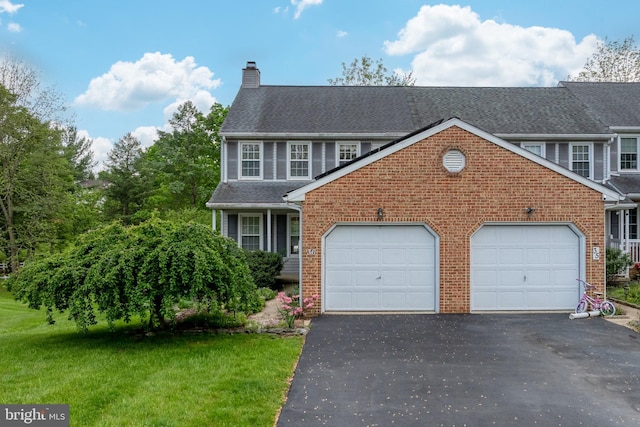 view of front facade featuring a chimney, driveway, brick siding, and an attached garage