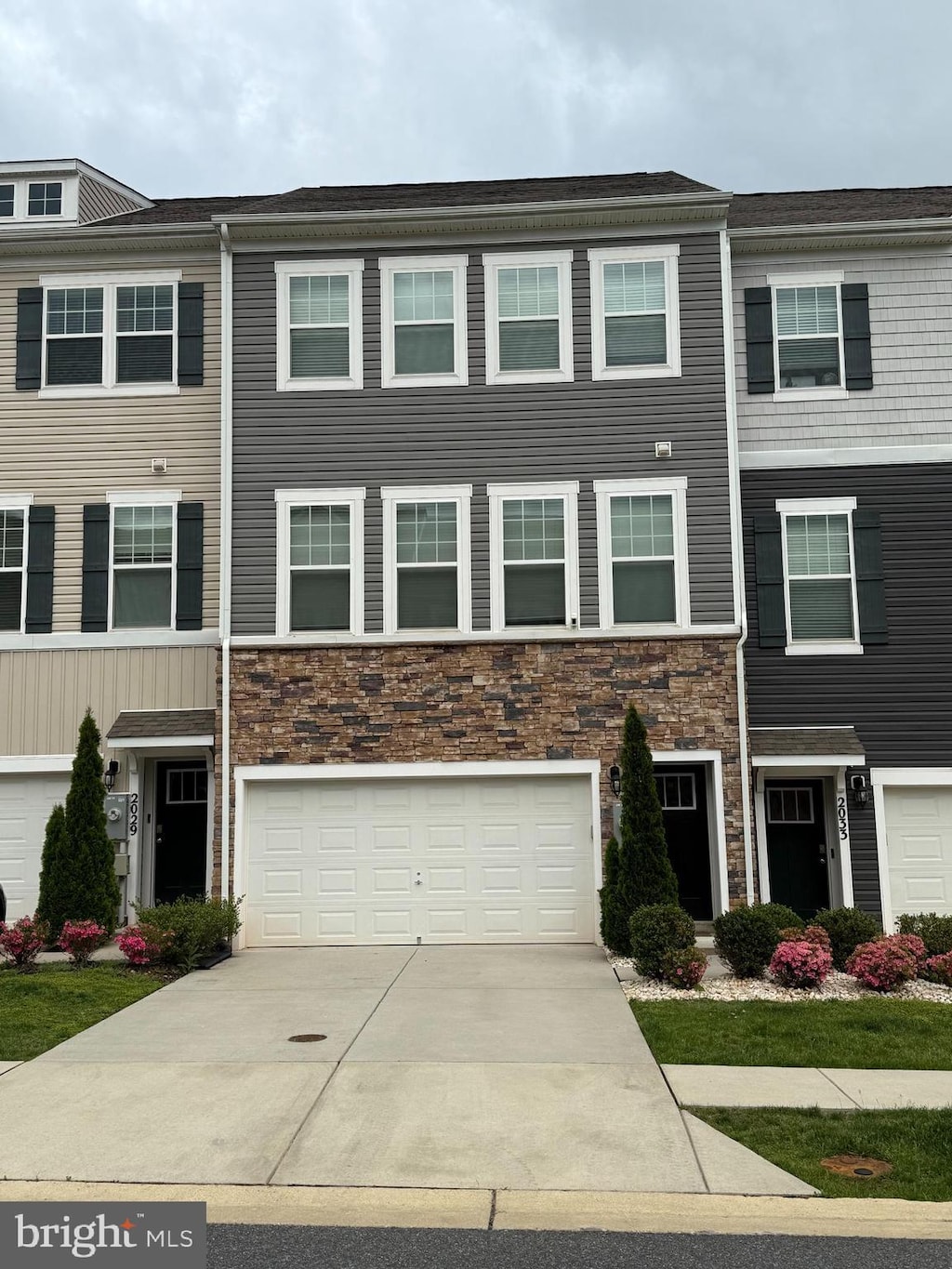 multi unit property with stone siding, driveway, and a garage