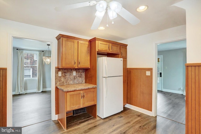 kitchen featuring freestanding refrigerator, a ceiling fan, a wainscoted wall, light wood-style floors, and light countertops