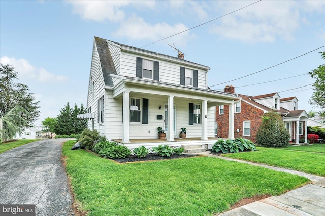 view of front of property with covered porch, a chimney, and a front yard