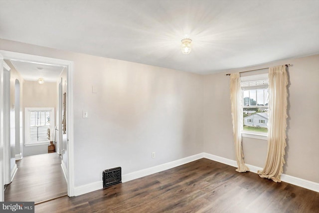 empty room featuring baseboards, dark wood-style floors, and visible vents