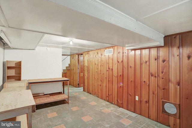 finished below grade area featuring wood walls, stairway, tile patterned floors, and visible vents
