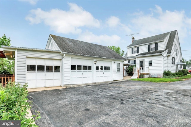 view of front of home with roof with shingles, a detached garage, a chimney, and an outbuilding