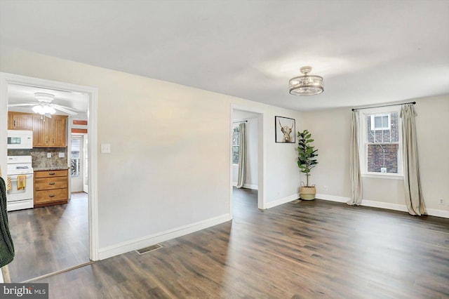 empty room with ceiling fan with notable chandelier, baseboards, dark wood-style floors, and visible vents