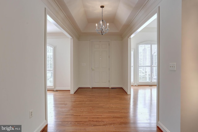 foyer entrance with a chandelier, light wood-style flooring, baseboards, and a tray ceiling