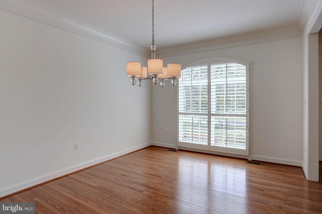 empty room featuring a chandelier, crown molding, hardwood / wood-style floors, and baseboards